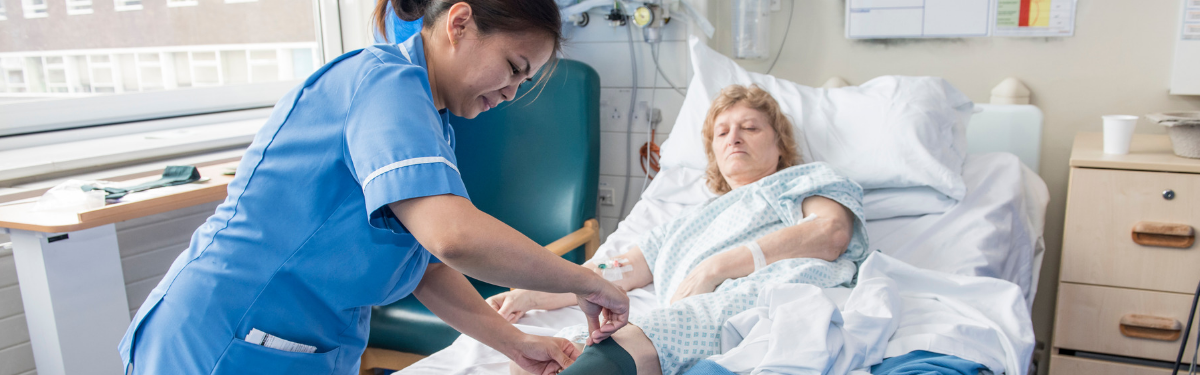 Healthcare assistant dressing leg for patient in hospital