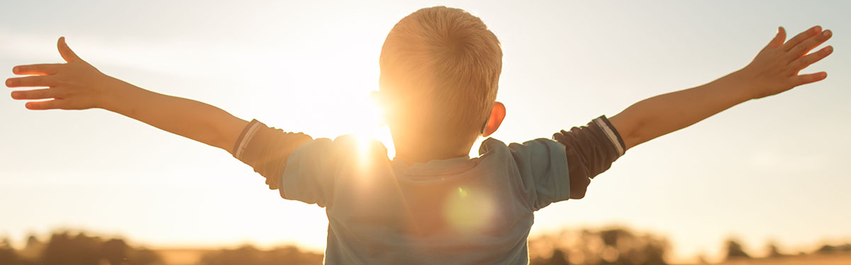 Child with arms outstretched towards sun
